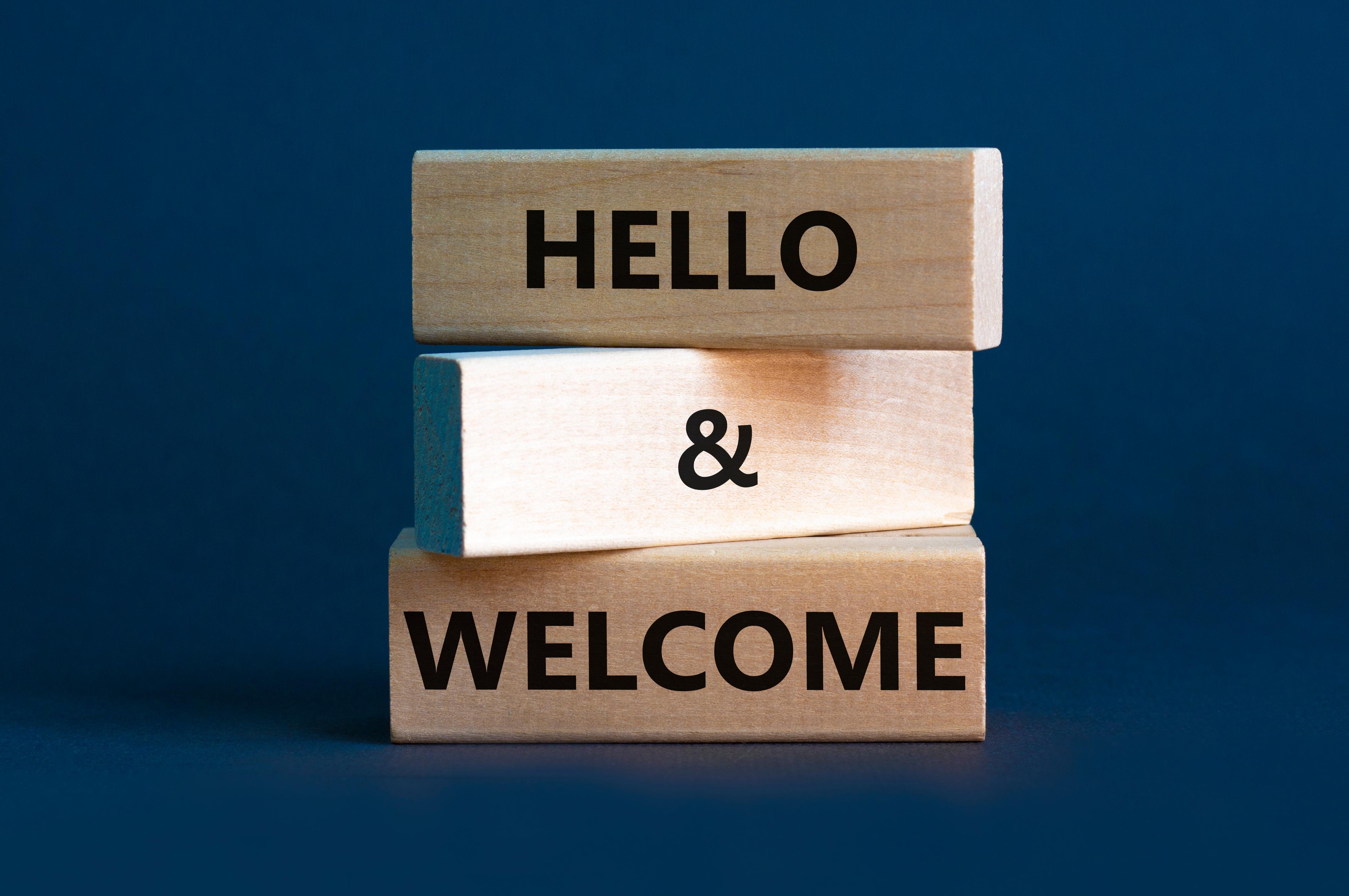 3 wooden blocks with the words 'hello and welcome' on them against a dark blue background.